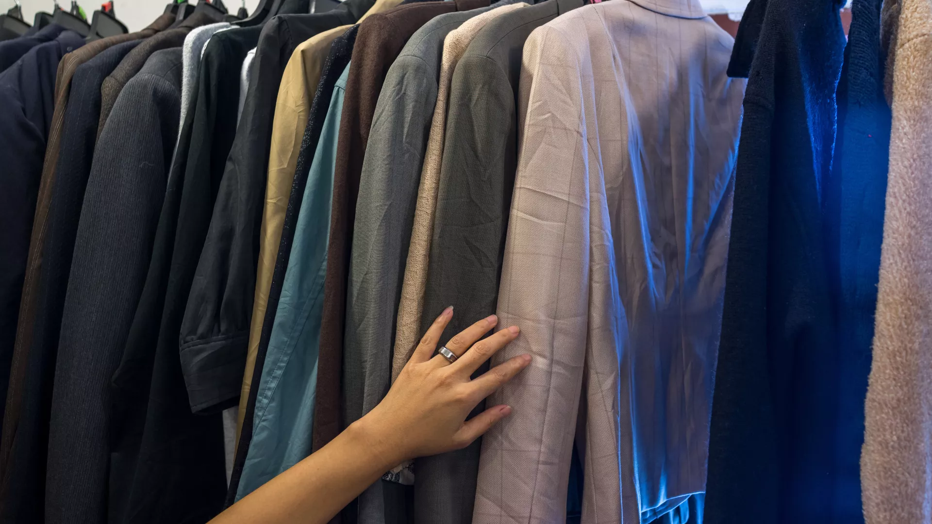 Female hand on male jackets on rack
